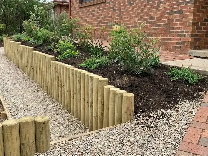 A palisade retaining wall of upright treated pine logs along a narrow side passage